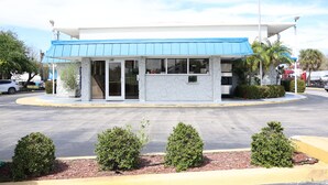 A small, single-story building with a blue awning, a marble facade, and a parking lot.