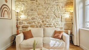 A living room with a stone wall, a beige sofa, two side tables, and a framed picture on the wall. - Superb AC Apartement Notre Dame de Paris (Paris)