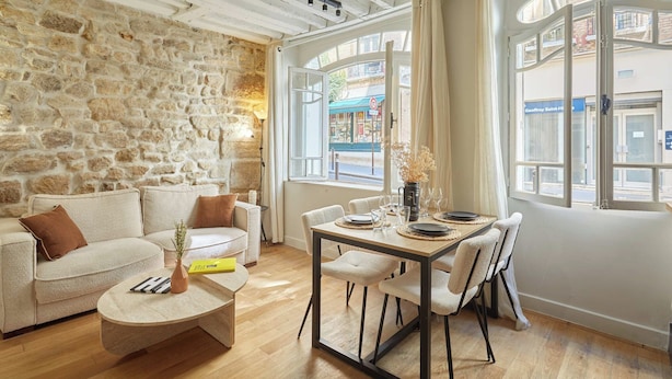 A cozy living room with a stone wall, a wooden dining table, and a sofa. - Superb AC Apartement Notre Dame de Paris (Paris)