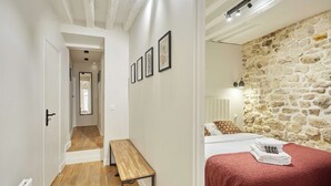 A narrow hallway leading to a bedroom with a stone wall, a wooden bench, and a bed with a red blanket. - Superb AC Apartement Notre Dame de Paris (Paris)