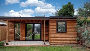 Une cabane en bois avec une porte coulissante en verre, un hamac et une petite fenêtre.
