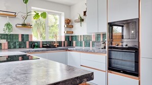 Une cuisine moderne dotée d’un grand îlot central, d’un four encastré et d’étagères en bois ornées de plantes.