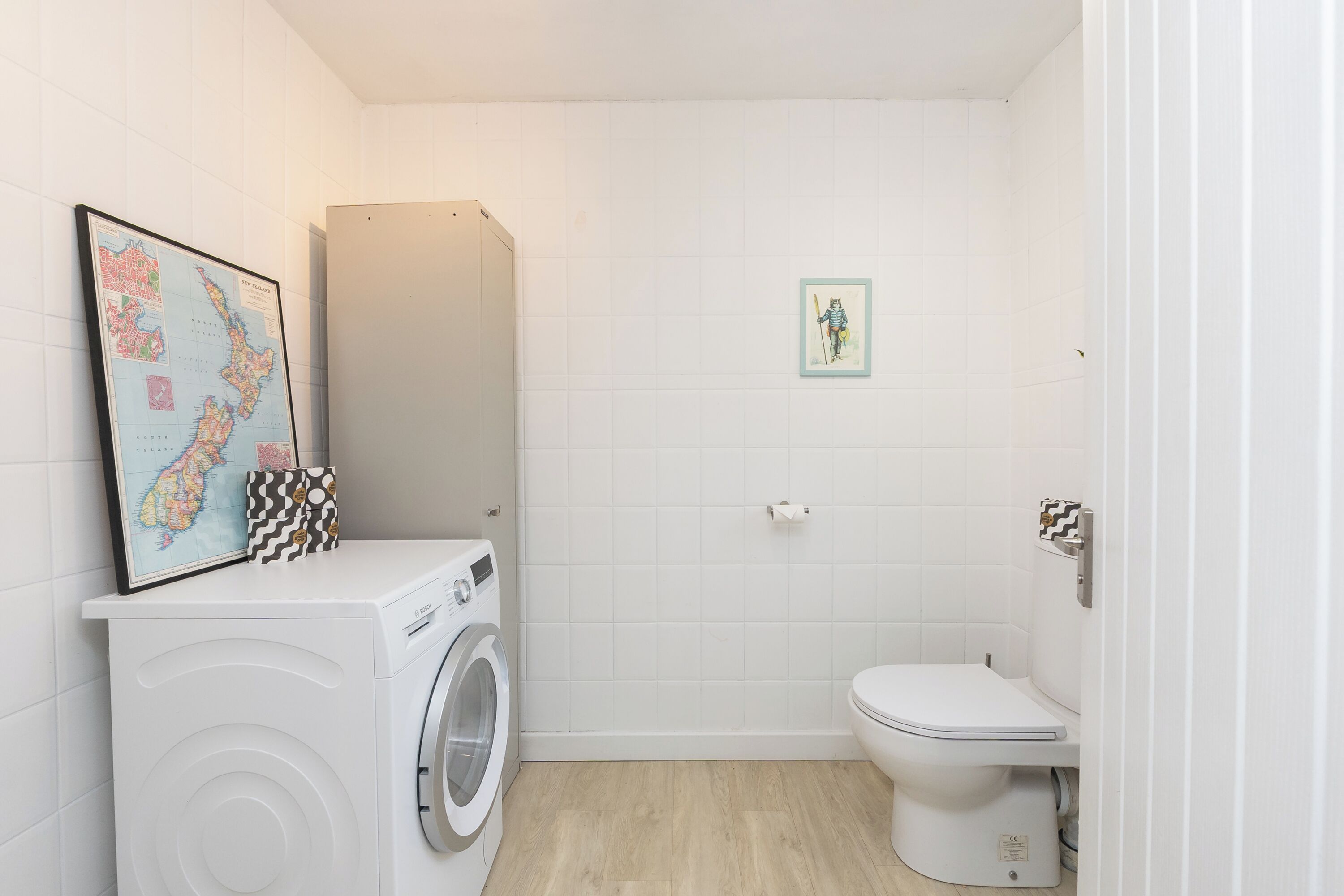 A small, clean bathroom with a washing machine, toilet, and a framed map on the wall.