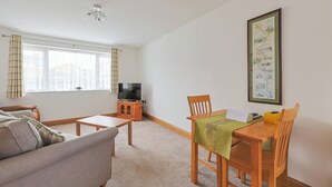 Ein Wohnzimmer mit einer Couch, einem Tisch und einem Fernseher auf einem Schrank.