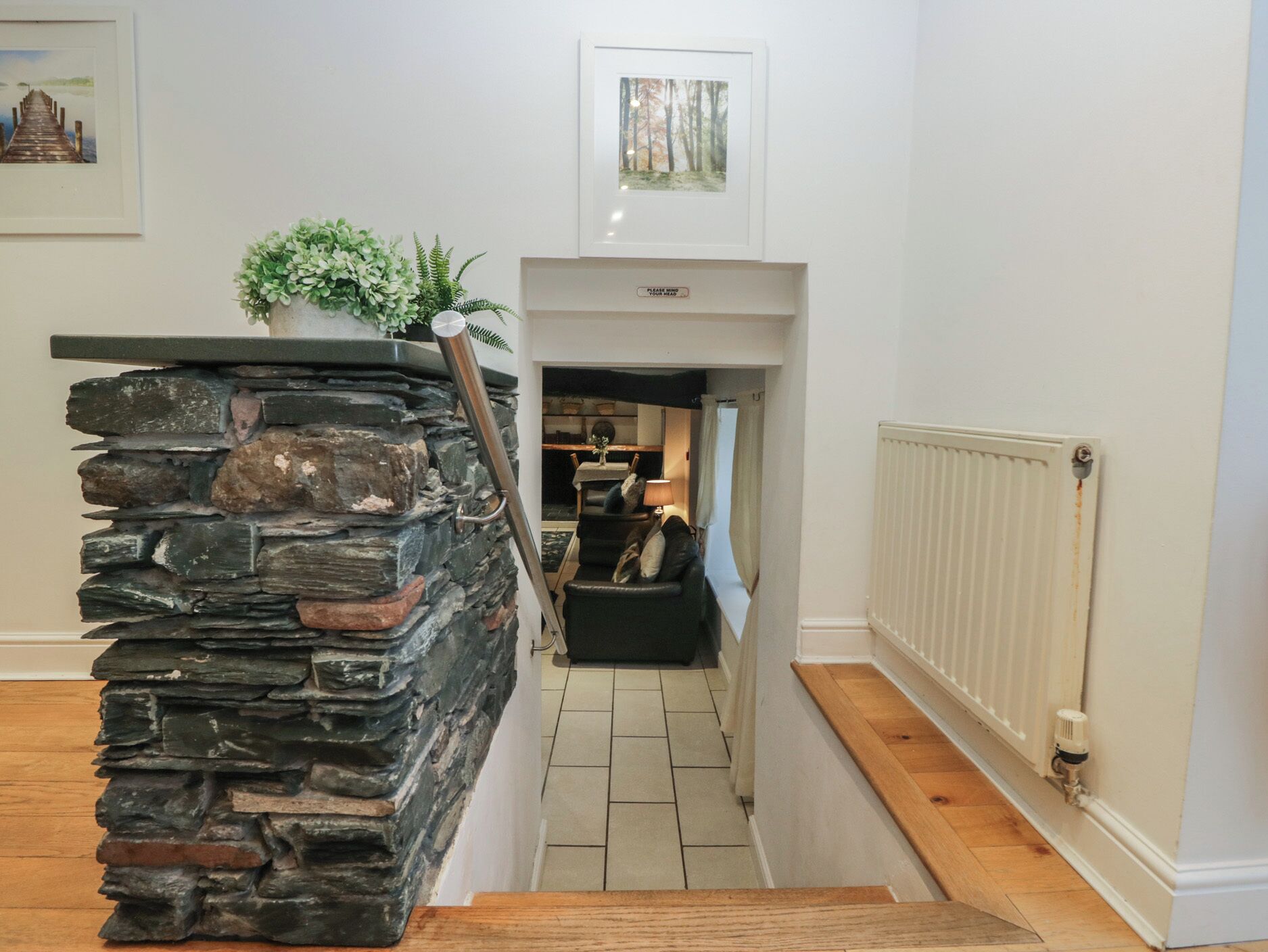 Una escalera con un muro de piedra y una planta en la parte superior, que lleva a una habitación con un radiador y una ventana.
