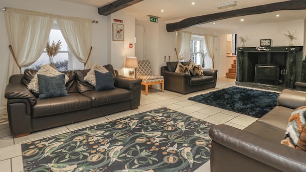 A spacious living area with leather sofas, a patterned rug, and a fireplace. - Newlands Fell House (Keswick)