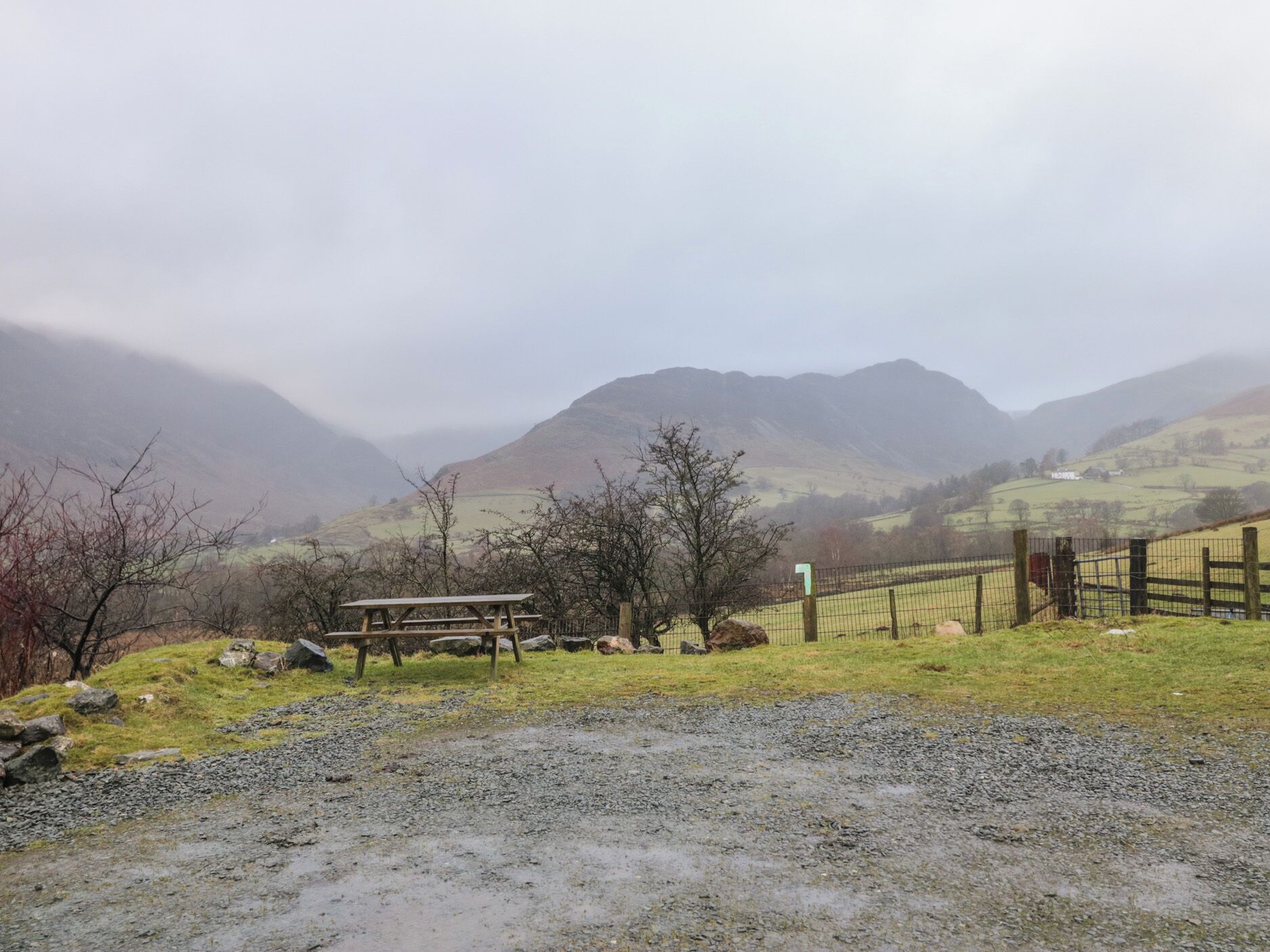 A rural landscape with a picnic table, a fenced area, and a mountain backdrop.