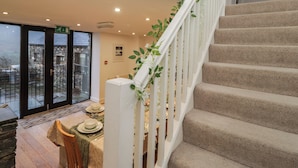 A staircase with beige carpeted steps and white railings, leading to a dining area with a table set for two. - Newlands Fell House (Keswick)