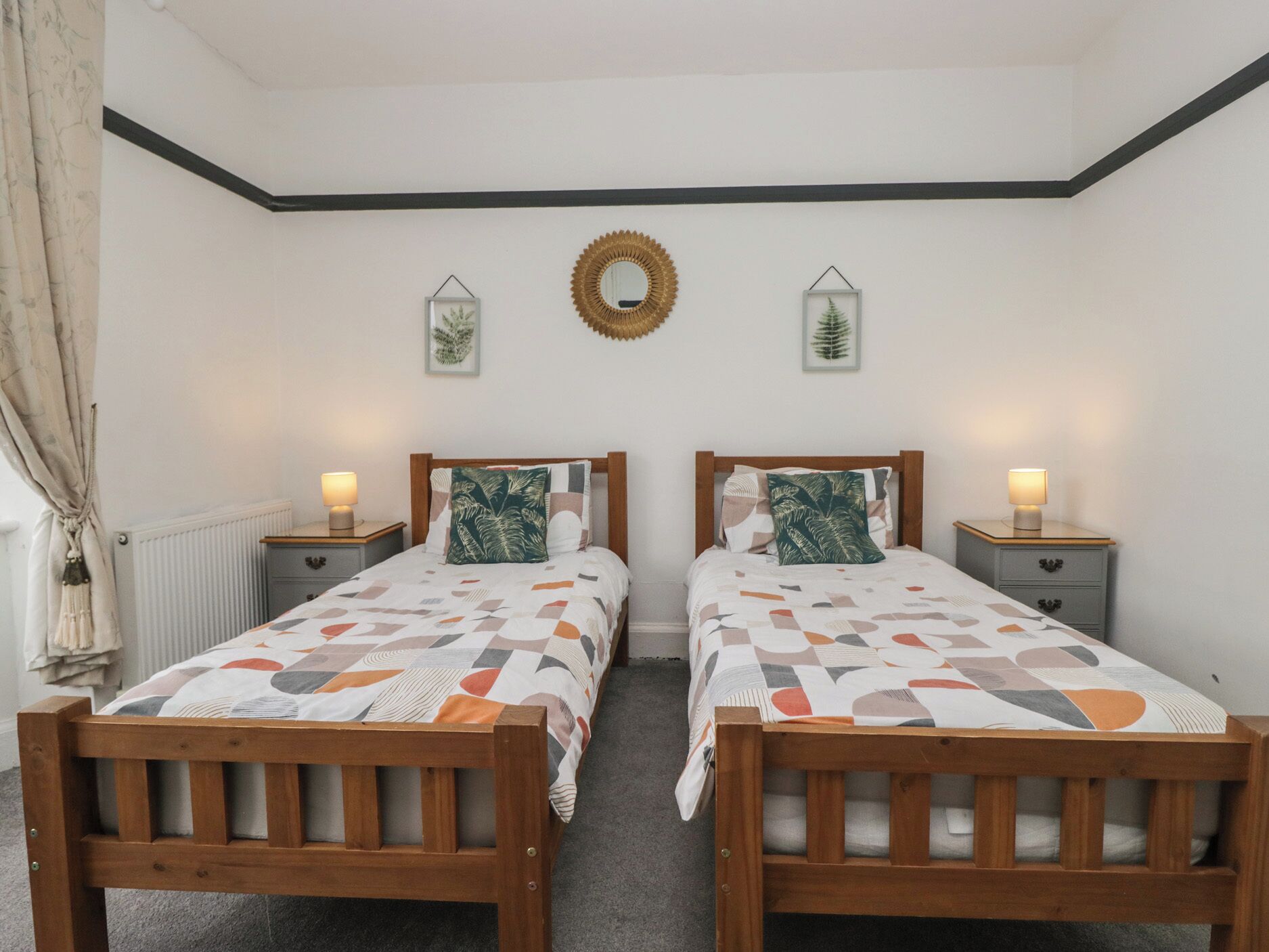 Una habitación doble con dos camas de madera, cada una con una mesita de noche y una lámpara. Hay dos adornos colgados en la pared sobre las camas.