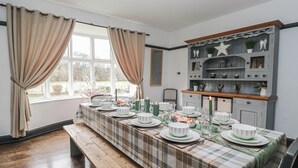 Ein Essbereich mit einem langen Tisch, der für eine Mahlzeit gedeckt ist, mit Vorhängen und einer dekorativen Schrankwand mit Regalen.