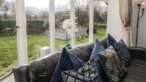 Ein Zimmer mit großem Fenster, einem Ledersofa und Blick auf einen Garten.