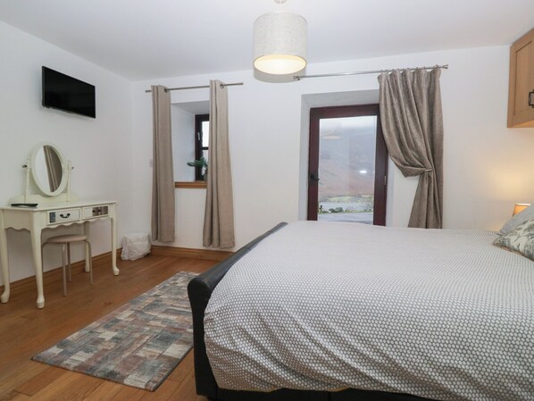 A bedroom with a bed, a dresser, a mirror, a television, and a window with curtains. - Newlands Cottage (Keswick)