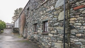 A stone building with two windows and a door, a paved path, and a gate in the background. - Newlands Cottage (Keswick)