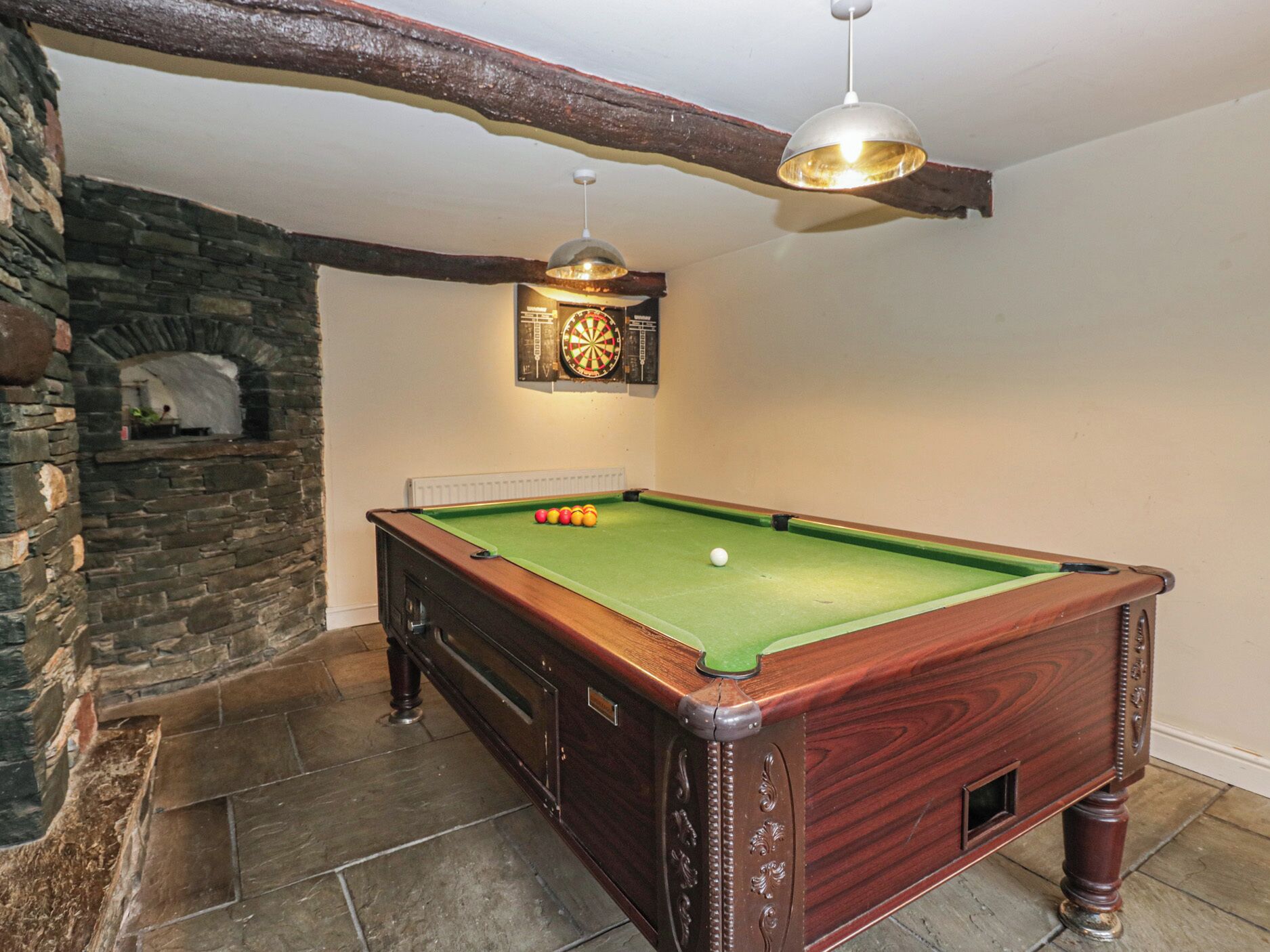 A pool table with balls, a dartboard, and a stone wall.