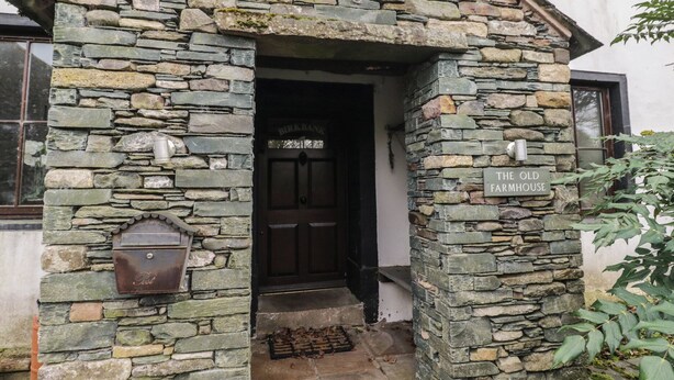 A stone farmhouse entrance with a wooden door labeled "BIRK BANK" and a sign reading "THE OLD FARMHOUSE". - Birkbank Farm (Cockermouth)