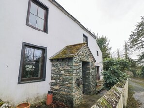 A white building with a stone extension, a window with white flowers, and a small door. - Birkbank Farm (Cockermouth)