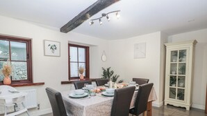 A dining area with a table set for six, surrounded by chairs. There is a window with a view of greenery outside, a radiator, and a cabinet with glass doors. - Birkbank Farm (Cockermouth)