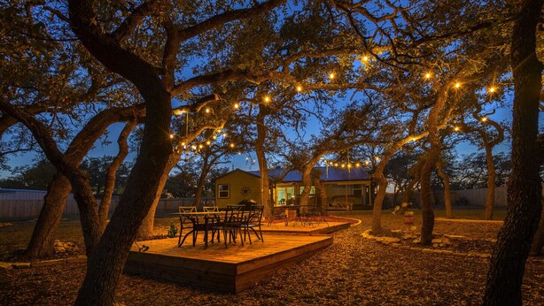 Un espace de restauration en plein air doté d’une terrasse en bois, entouré d’arbres et illuminé de guirlandes lumineuses.