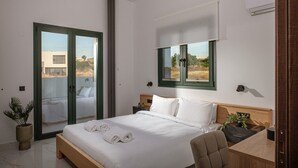 Moderni hotellihuone, jossa on sänky, työpöytä, tuoli, ruukkukasvi ja näkymä ulos.