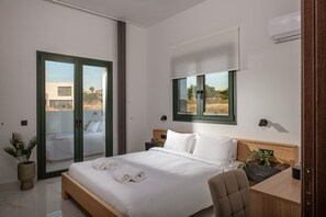 A modern hotel room with a bed, a desk, a chair, a potted plant, and a view of the outdoors. - Villa Sol: Luxury Living in Heart of Gournes (Gournes Gouvon)