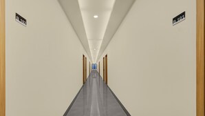 A long, narrow hallway with a polished floor, wooden doors on either side, and ceiling lights.