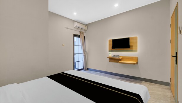 A modern hotel room with a bed, a mounted TV, and a window with curtains.