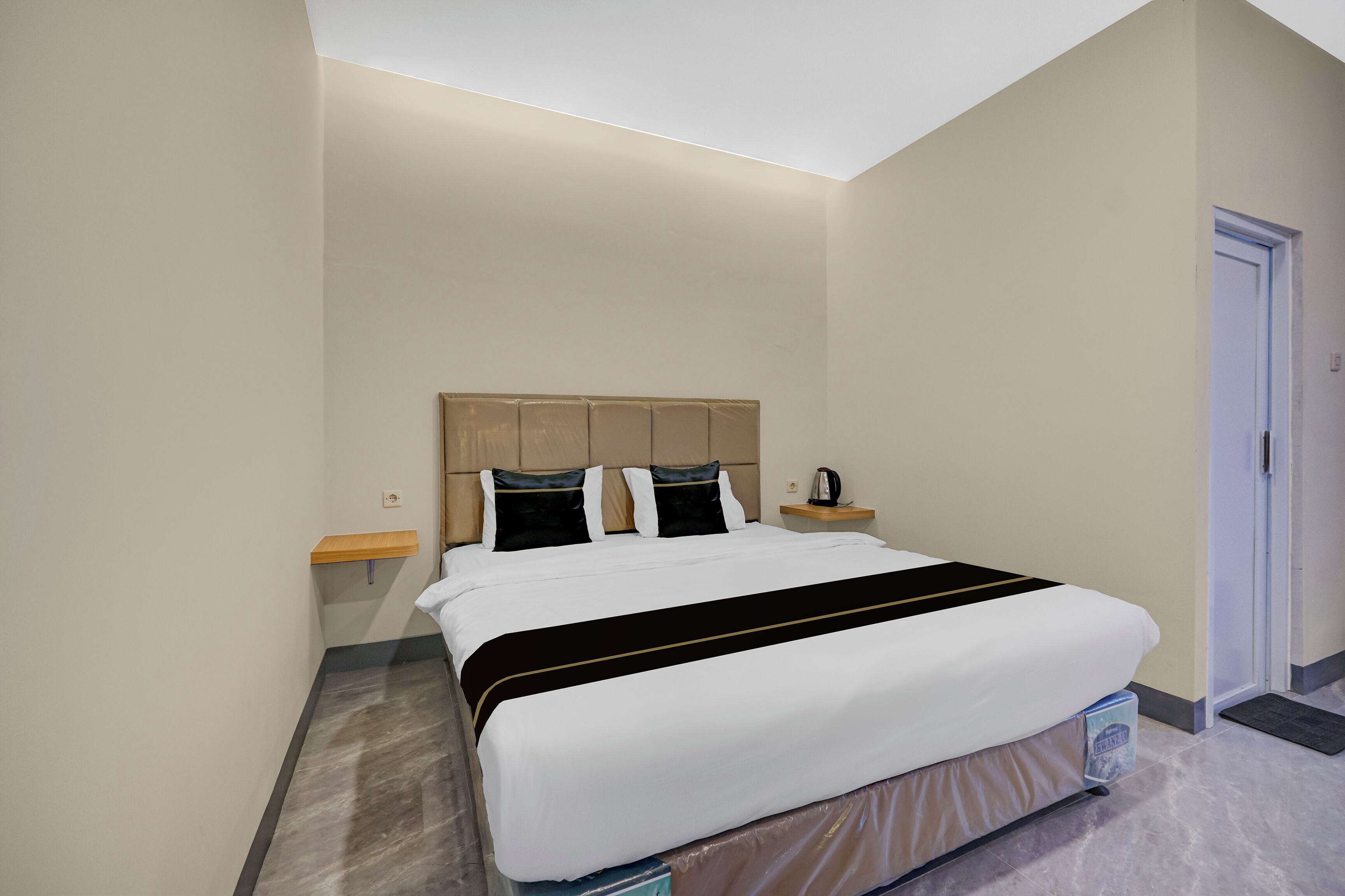 Een hotelkamer met een bed, nachtkastje, plank en een deur.
