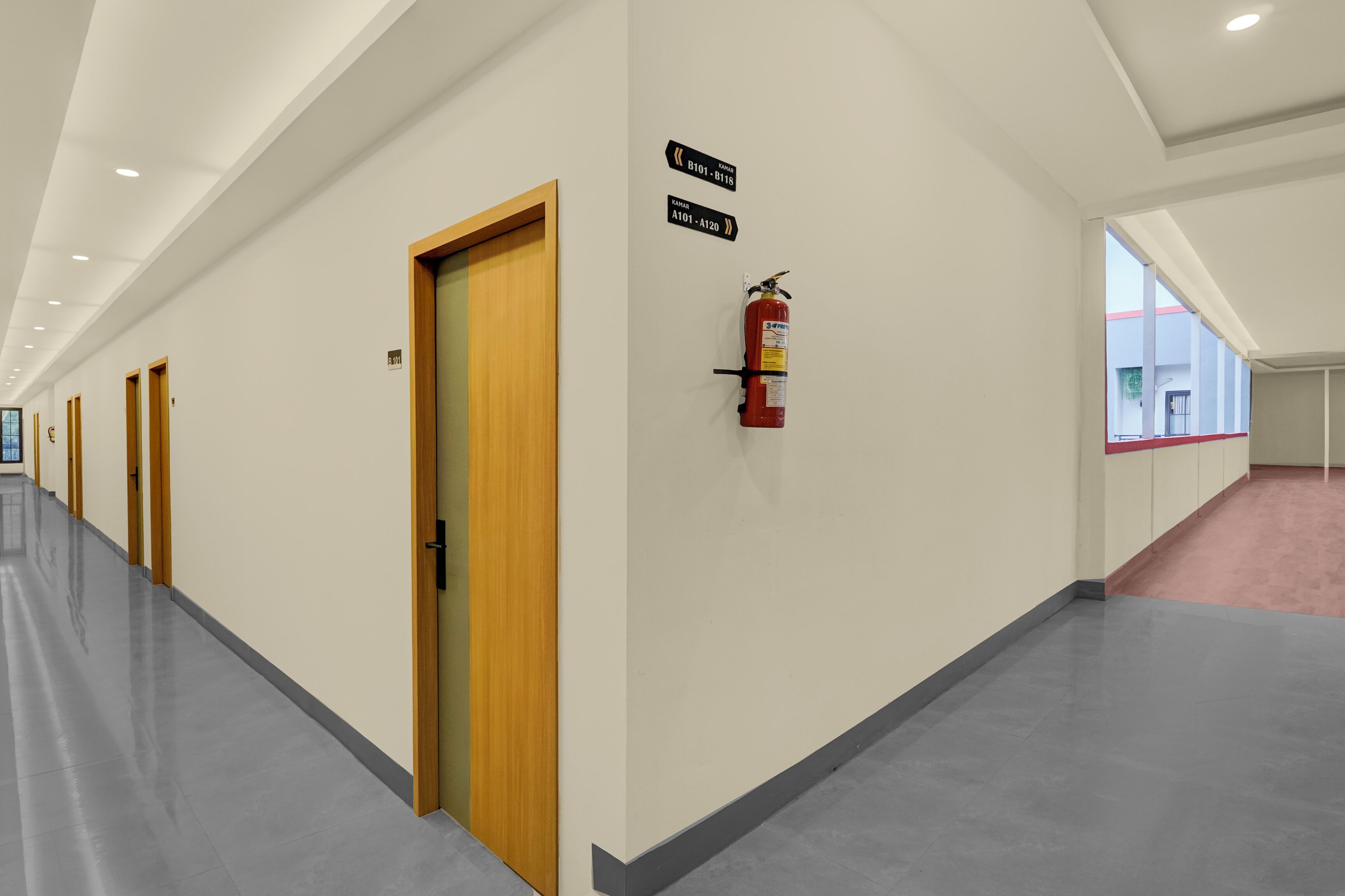 A hallway with doors, fire extinguisher, and directional signs.
