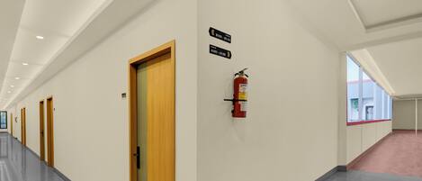 A hallway with doors, fire extinguisher, and directional signs.