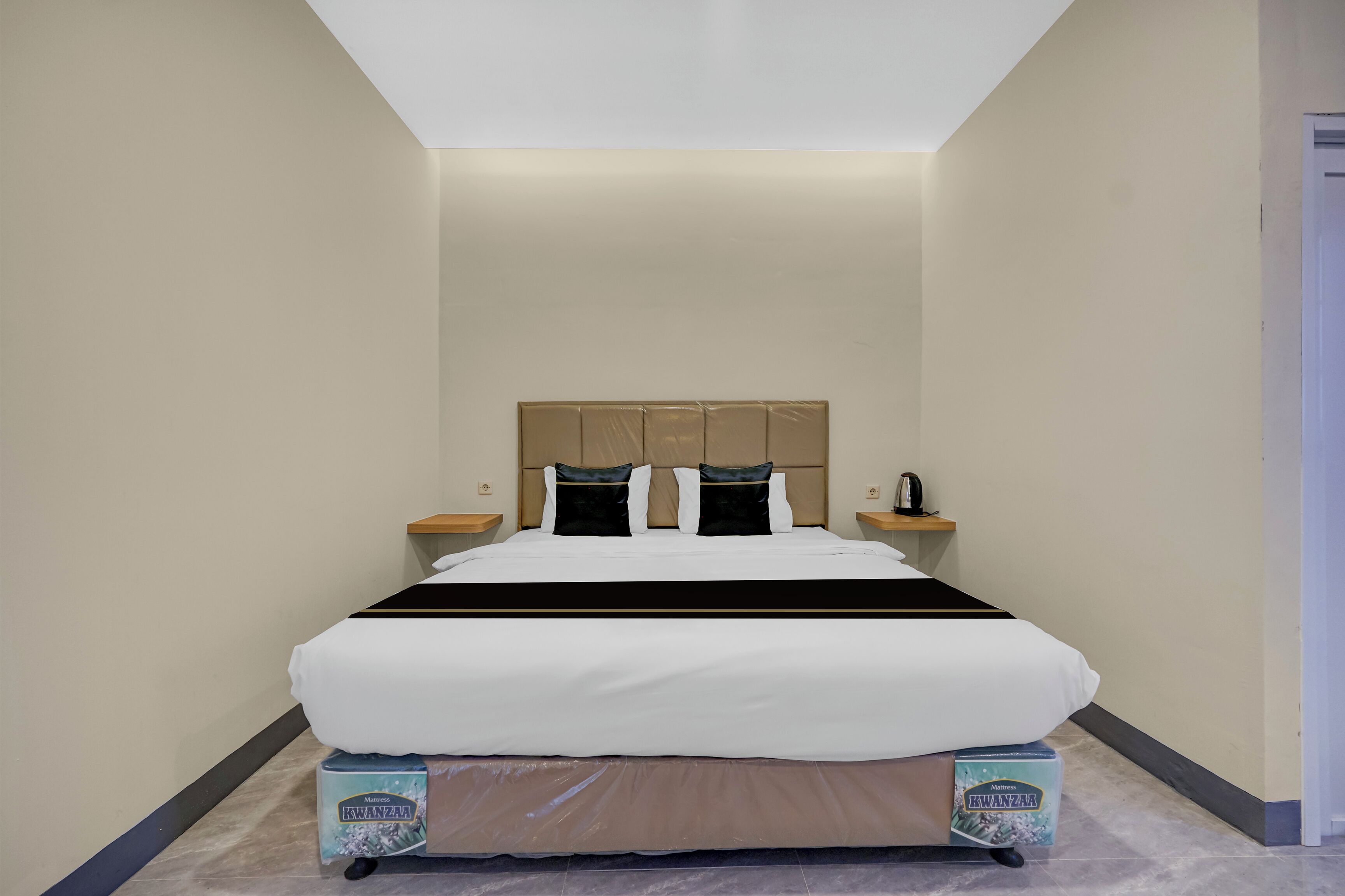 Una cama bien hecha con cabecera, dos mesitas de noche con lámparas y una caja de adornos de Kwanzaa en el suelo.