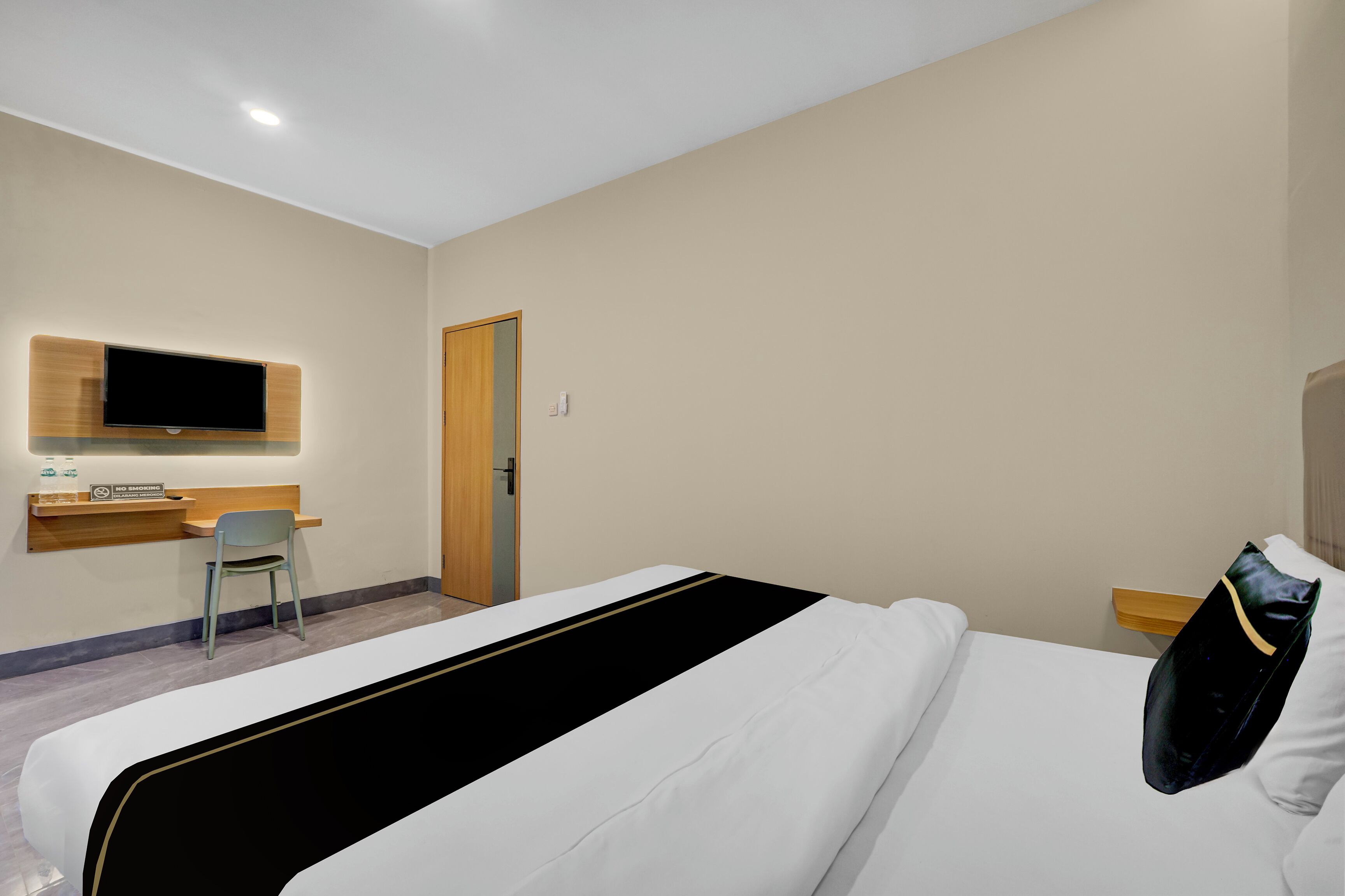 A hotel room with a bed, a desk with a chair, a television mounted on the wall, and a door.