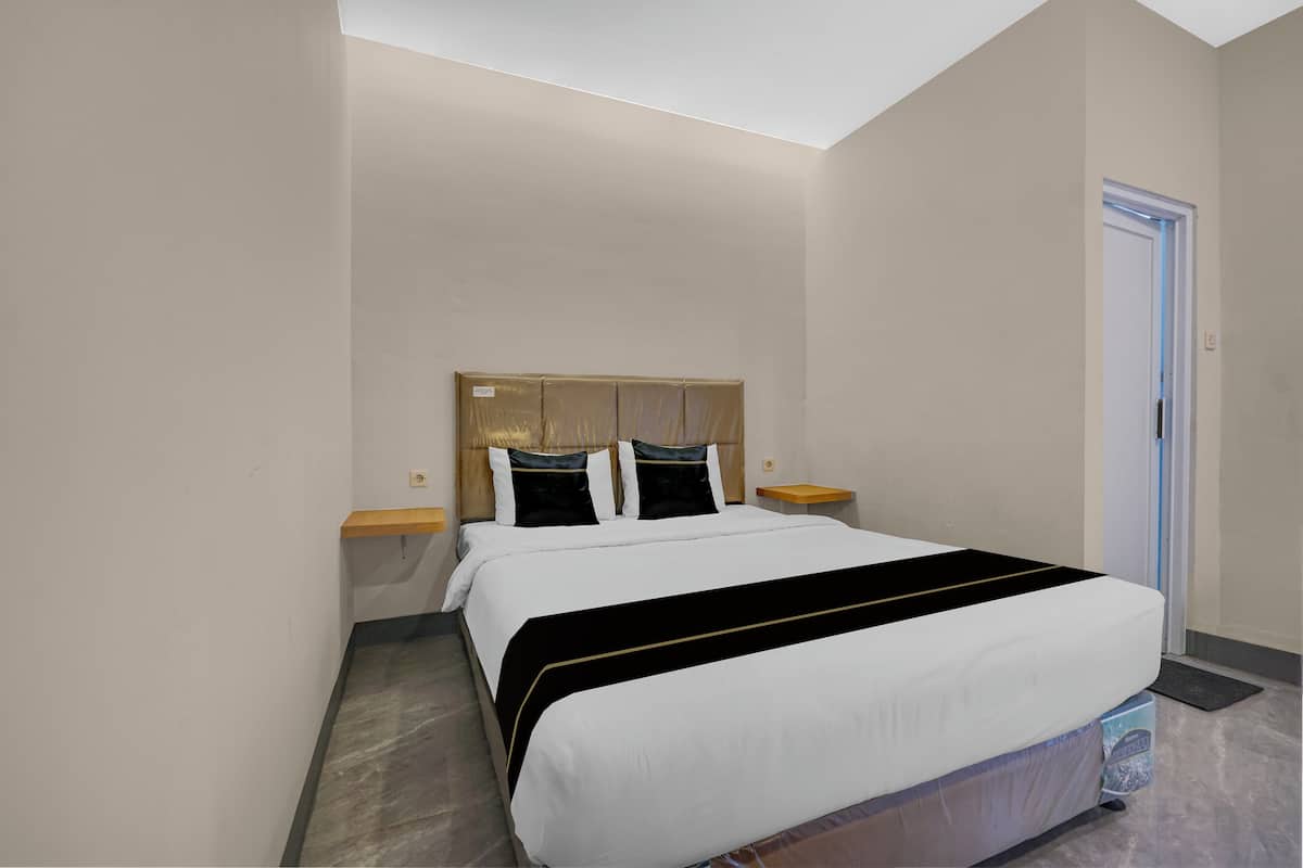 Une chambre d’hôtel avec un grand lit, une tête de lit en bois, deux tables de chevet et une porte.