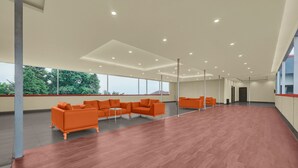 A spacious room with a wooden floor, orange sofas, and large windows.