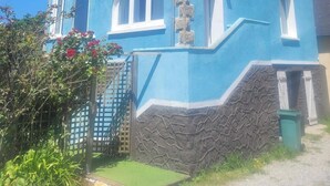 Ein zweistöckiges Haus mit steilem Giebeldach, einem Steinkamin und einer kleinen Veranda mit Holzgeländer.