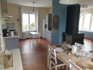 A cozy kitchen with a dining area, a black wood-burning stove, and a view of the outdoors. - ADONIS'S HOUSE in Telgruc (Telgruc-sur-Mer)