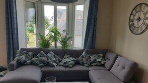 Ein modernes Wohnzimmer mit einem grauen Ecksofa, einem Glastisch und einer großen Wanduhr.