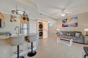A modern kitchen with a built-in oven, a refrigerator, and a sink. There is a dining area with a sofa and a coffee table. - Waterview 4th Floor Condo | Heated Pool & Hot Tub (St. Petersburg)