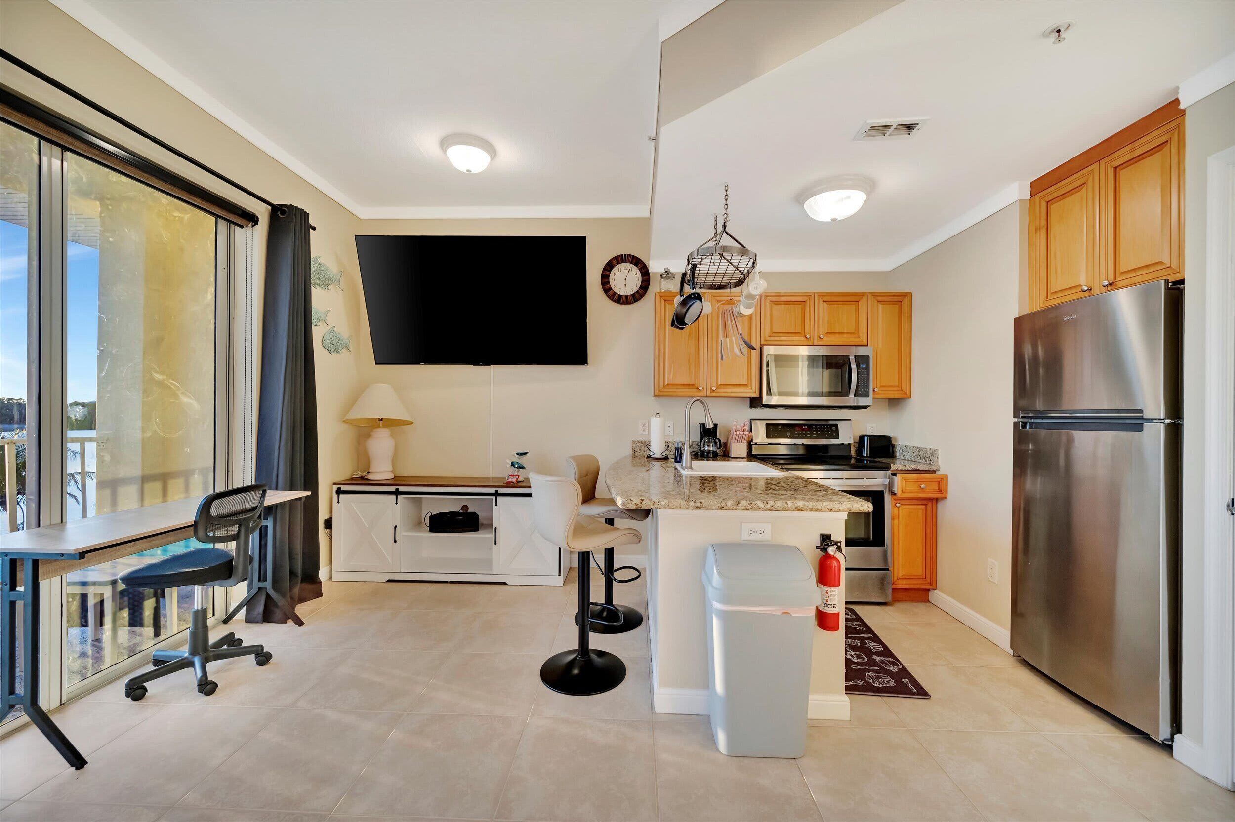 A modern kitchen with a large island, stainless steel appliances, wooden cabinets, and a sliding glass door leading to a balcony.