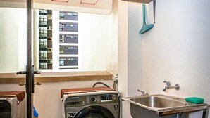 Un espacio pequeño para lavandería con lavadora, lavamanos y un balde.