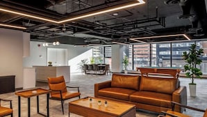 A modern office space with a leather sofa, wooden coffee table, and a dining area with chairs and a table. - Steps to Nightlife & Dining, Gym, Sauna, Stampede (Calgary)