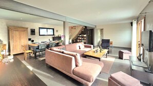 A modern living room with a large sofa, a coffee table, and a television. There is a staircase leading to a loft area with a desk and shelves. - Spacious family home near Vannes, Terémer (Saint-Nolff)