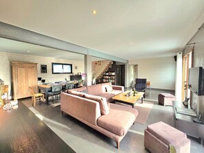 A modern living room with a large sofa, a coffee table, and a television. There is a staircase leading to a loft area with a desk and shelves. - Spacious family home near Vannes, Terémer (Saint-Nolff)