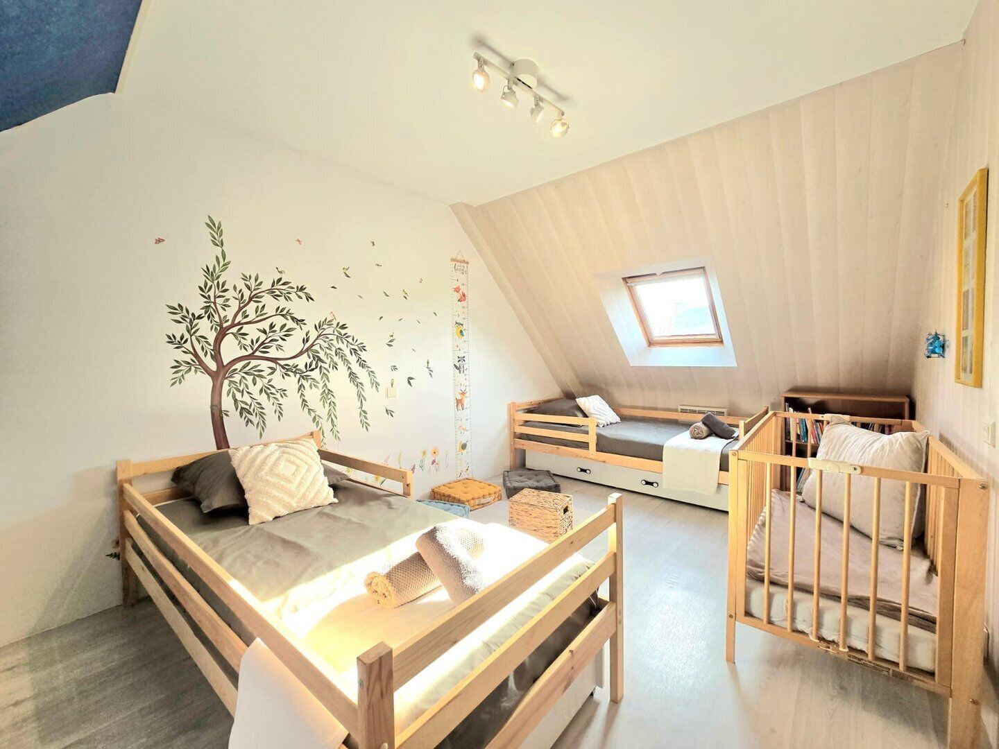 Une chambre mansardée chaleureuse et bien éclairée, avec un plafond en pente, un lit en mezzanine, un berceau et une petite fenêtre.