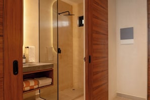 A modern bathroom with a glass-enclosed shower, wooden cabinetry, and a built-in shelf with towels. - Elements 326 (Tulum)