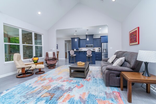 A modern living room with a sofa, a recliner, a coffee table, and a lamp. There is a kitchen area with blue cabinets and a microwave. - Steps to Fairway: Hot Springs Village Golf Retreat (Hot Springs Village)