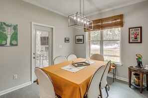 Un comedor con una mesa preparada para cuatro personas, una araña y una ventana con persianas.