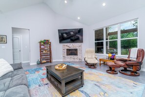 A living room with a fireplace, a large TV, leather chairs, and a colorful rug. - Steps to Fairway: Hot Springs Village Golf Retreat (Hot Springs Village)