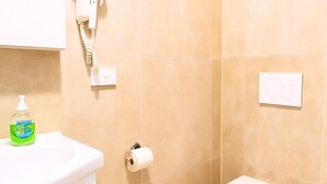 Ein Badezimmer mit Toilette, Seifenspender, Toilettenpapierhalter und einem an der Wand befestigten Telefon.