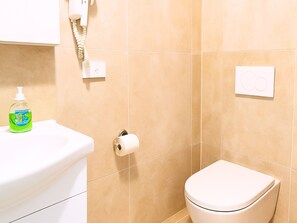 A bathroom with a toilet, a soap dispenser, a toilet paper holder, and a wall-mounted phone. - Magnolia Apartment (Venezia)