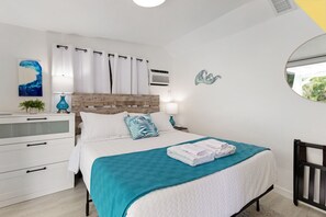 A modern bedroom with a wooden headboard, white bedding, a teal throw blanket, and a bedside table with a lamp. - Private Pool, Bar, Putt Green, Jet Tub, King Bed, quiet town 5min drive to beach (Pompano Beach)
